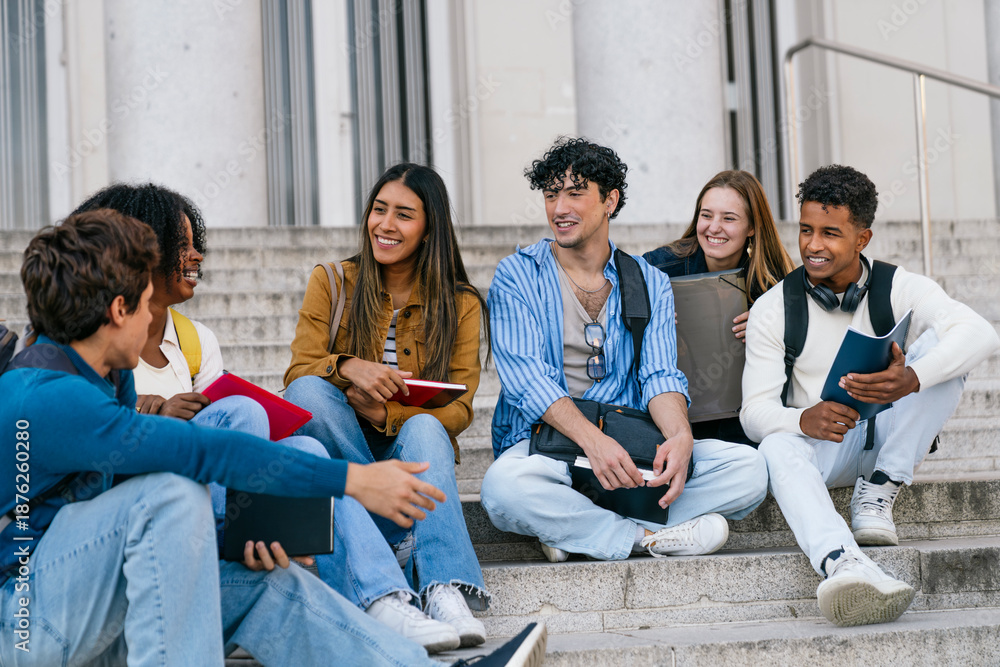 Obraz premium Group of diverse university students smiling and chatting happily while sitting on campus stairs outside the building