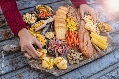 Different types of uncooked pasta at the hands of two women in the wood bowls.