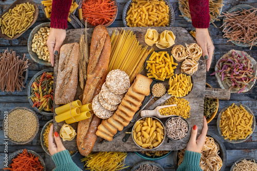 Different types of uncooked pasta at the hands of two women in the wood bowls.