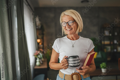 Schilderij op canvas Portrait of senior mature woman stand and hold cup and book at home