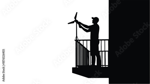 Person silhouetted on balcony assembling a small wind turbine against a white sky