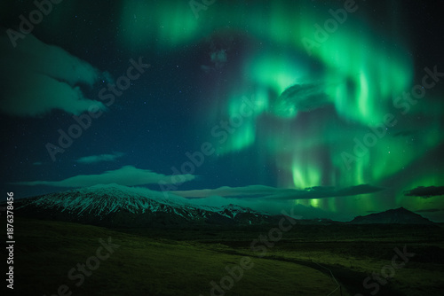 View of the vibrant aurora borealis dances above the snow-dusted mountains, casting an ethereal glow on the dark Icelandic landscape, Grundarfjordur, West Iceland, Iceland.