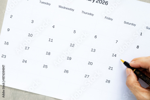 Person hand marking Valentine's Day on February 2026 calendar with pen, Planning romantic date or anniversary celebration, High angle view of calendar page with space for text.