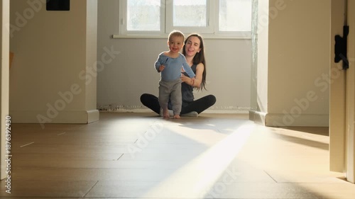 a child toddler with bare legs runs away from mother's arms across the floor against a sunny window, hugging mom happy family first steps towards his family at the window of the house