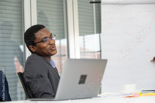 A black man wearing glasses is sitting in front of a laptop.