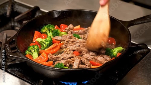 A chef skillfully stirs sizzling beef and vibrant vegetables in a cast-iron skillet on a commercial stove, creating a delicious stir-fry dish in a busy kitchen environment