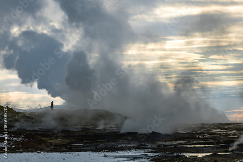 Wallpaper Mural View of geothermal steam rising from the dark, textured earth, a solitary figure amidst the otherworldly landscape, under a sky streaked with dawn, Rejkjahlid, North Iceland, Iceland. Torontodigital.ca