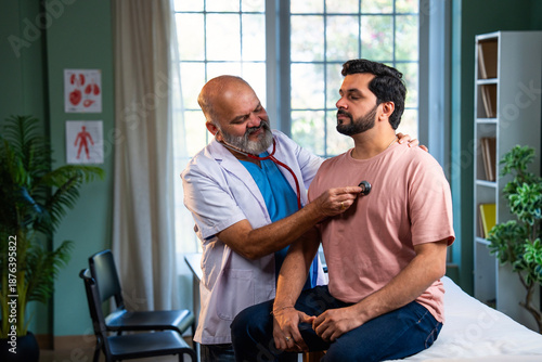 Senior Indian physician uses medical torch to examine young male patient in modern clinic