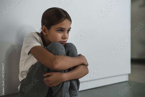 Fotografie Close-up portrait of young girl curled up against white wall feeling deep sadnes