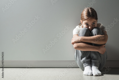 Vulnerable child curled up against gray wall feeling despair stress needs for protection