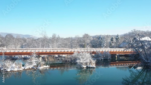 Wooden bridge over Mreznica River in village of Belavici in Croatia, snow on river banks, waterfalls and tree branches, idyllic rural winter landscape