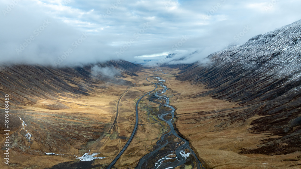 Obraz premium Aerial View of Remote Icelandic Valley with Meandering River and Mountain Road Surrounded by Mist and Volcanic Highlands
