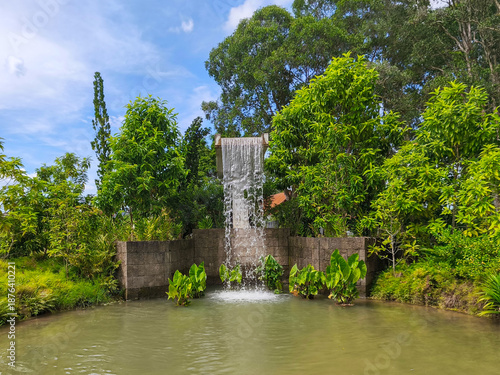 Canvas Print A cascading waterfall flows over a man-made stone structure into a tranquil pond