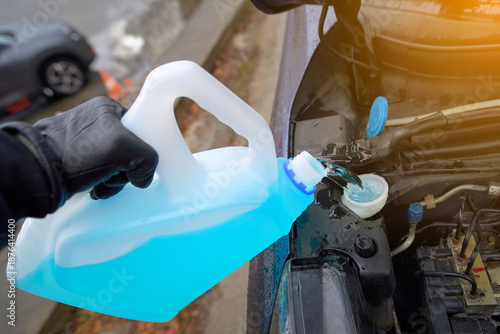 Foto Gloved hand pours bright blue winter screen wash fluid into cars open washer reservoir, cold weather preparation, protecting visibility against frost, ice on crisp