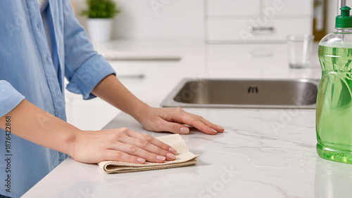 woman cleaning kitchen, Housework is done with care, Cleaning supplies are ready nearby, Microfiber works best for dust, The kitchen is very bright, The table is now dry, 