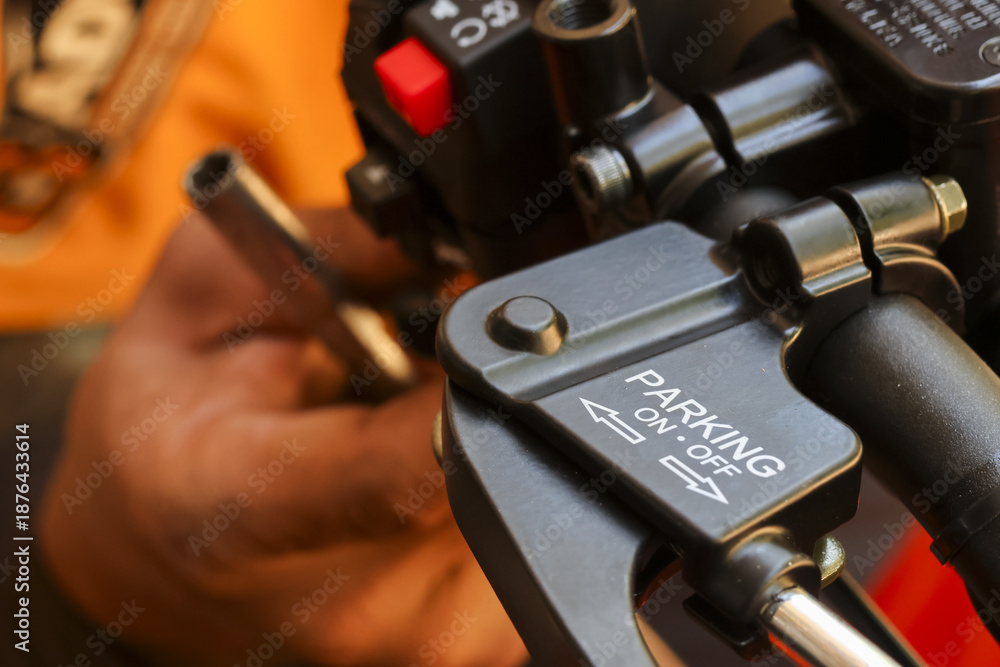 Naklejka premium Close up view showing focused maintenance check motorcycle handlebar parking brake lever mechanism featuring clear white lettering with mechanic hand blurred warm orange background working