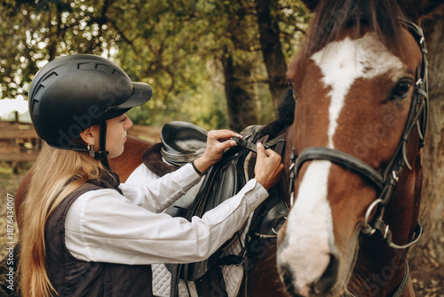 Fotografía A young woman jockey adjusts the harness on her horse before training