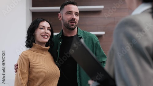 Couple engaged in a real estate transaction, smiling and interacting with an agent, exchanging documents and keys in a modern office setting with neutral colors and stylish decor