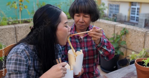 Asian mother and daughter eating together instant noodles outdoor at home terrace - Family lifestyle, culture and food concept