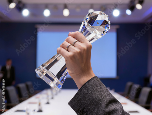 Close-up of a hand holding a sparkling glass crystal trophy high in a modern conference room background, symbolizing business achievement, excellence, and corporate victory.
