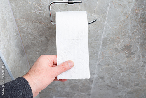A man takes white toilet paper in his hand. Close-up of a residential building restroom, bathroom.