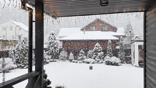 Winter returned in the middle of spring. It is snowing heavily with large snowflakes. Snow covers roofs, trees and the ground. Abnormal precipitation. View from the wooden terrace of the cottage
