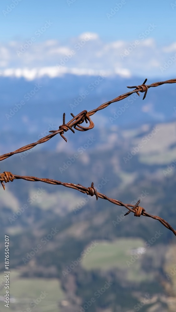 Obraz premium Rusty barbed wire fence against snowy alpine mountains and blue sky panorama.