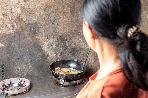 Quadro su tela Back view of a woman cooking in a humble kitchen