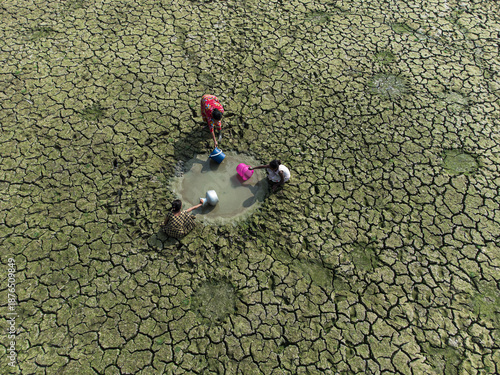 Rajshahi, Bangladesh - 14 April 2024: Aerial view of women collecting water from a scarce puddle in a cracked, parched landscape under the dry season sun.