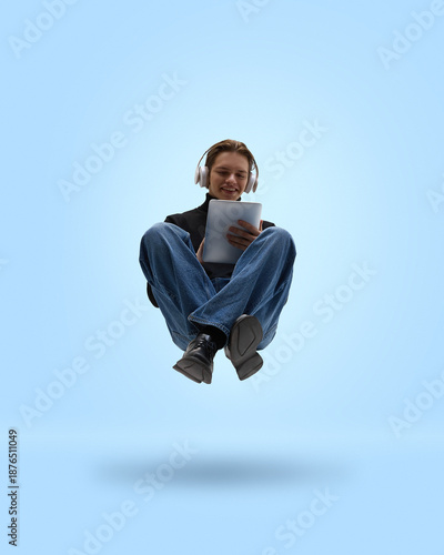 Fotografie Casual man levitating with tablet and headphones on blue background