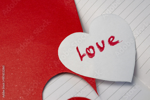 Red inscription love on a white cut paper heart
