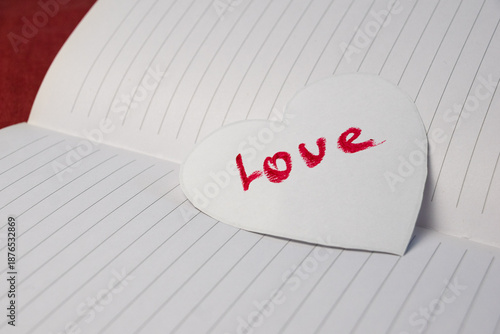 Red inscription love on a white cut paper heart