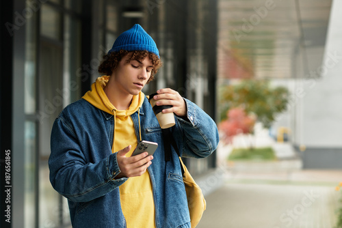 Curly teenager in a blue beanie enjoying coffee outdoors on a cool autumn day