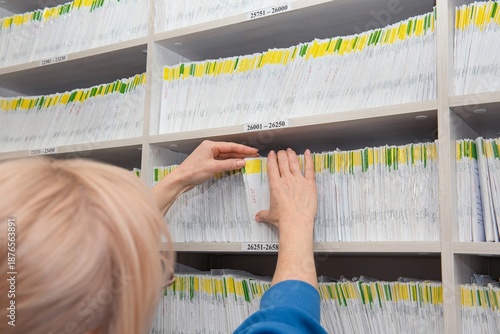 The girl's hands select a medical record with the correct number. View from behind.