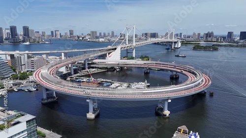 Flight over Rainbow Bridge loop interchange in Tokyo Bay with urban skyline and traffic