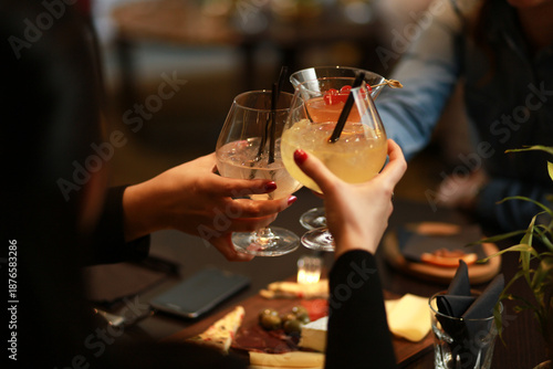 Friends toasting with gin and tonic cocktails in a modern, upscale bar. Lifestyle photography capturing a social gathering, celebration, and luxury nightlife atmosphere with blurred background lights.