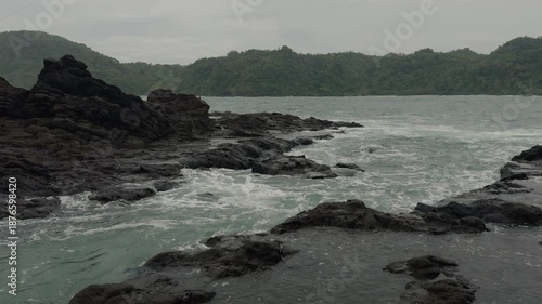 Landscape of the coastal area of Wediombo Beach with hills, trees, and massive coral rocks, in cloudy weather in 4K. A travel destination in Yogyakarta, Java, Indonesia, Asia.