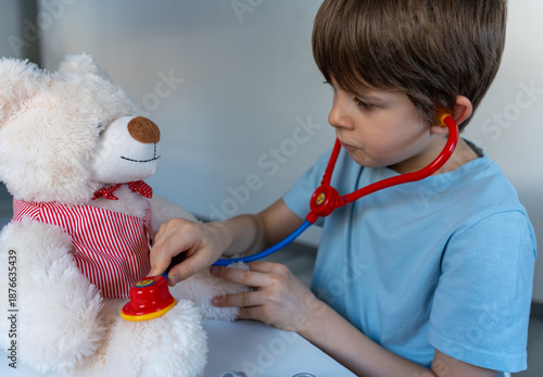 Fotografie Child playing doctor and examining teddy bear with stethoscope