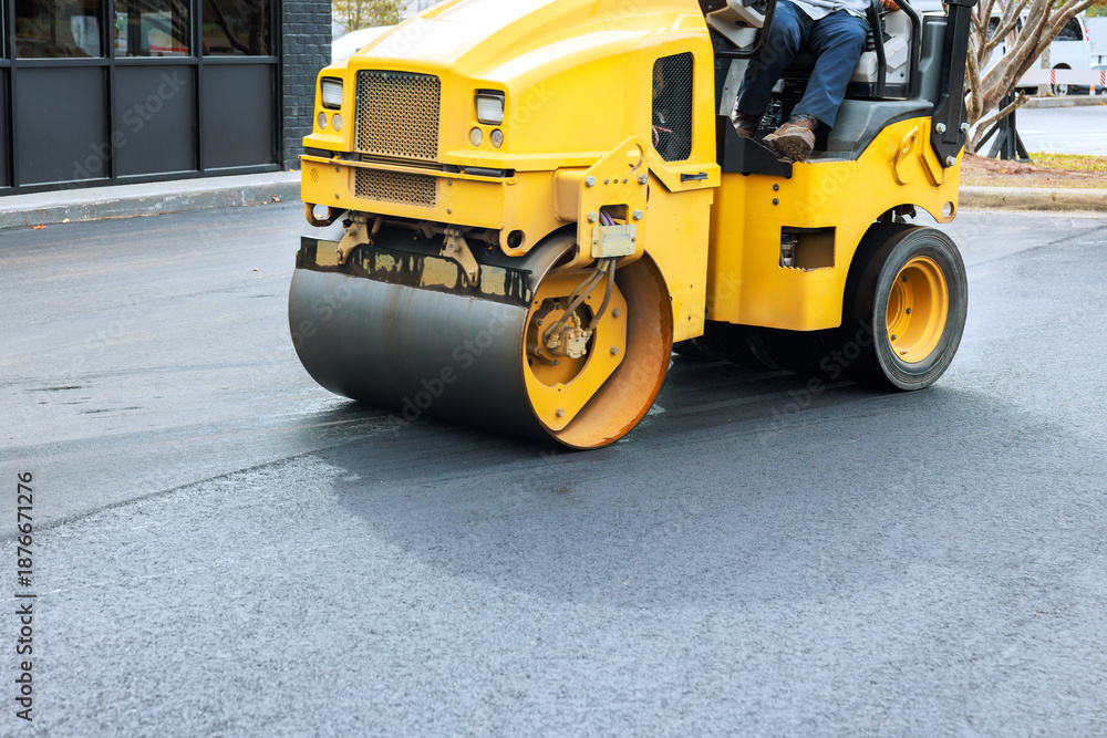Naklejka premium Yellow steamroller machine is flattening fresh asphalt at construction site