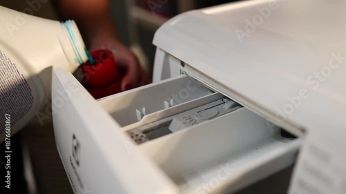 Woman pours necessary amount of liquid laundry detergent into compartment of washing machine from big bottle. Household chores concept. High quality FullHD footage