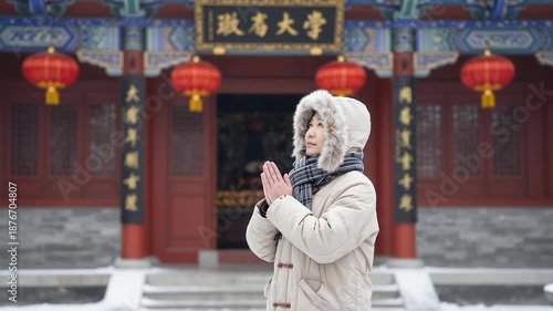 Woman in winter clothes making a wish at traditional Chinese temple in snow