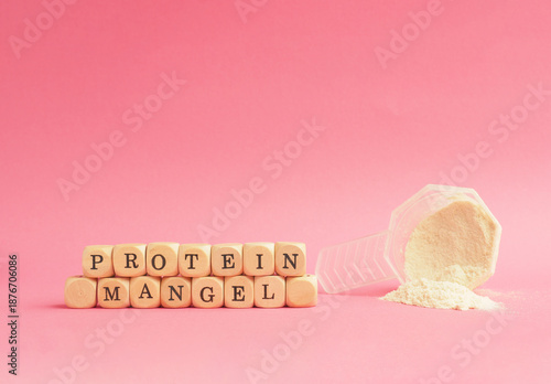 Small wooden cubes with the German inscription protein deficiency and a measuring spoon with protein powder on a pink background, food supplements, healthy eating, bio hacking
