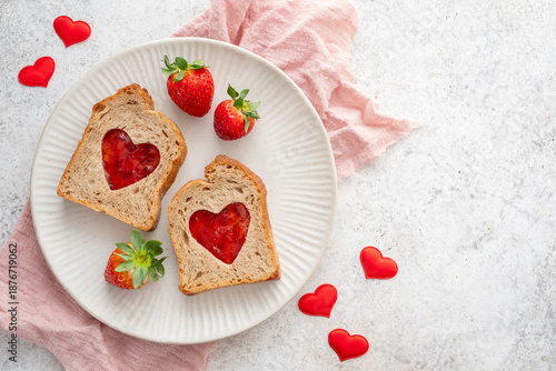 Toast with heart-shaped cutouts filled with jam and fresh strawberries on a plate with red heart decorations