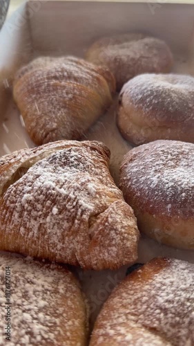 Slow motion video showing powdered sugar being gently sprinkled over traditional Neapolitan sfogliatelle pastries. The fine sugar falls delicately onto the flaky, golden layers, enhancing texture 