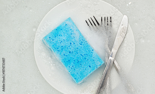 Washing dishes with blue cleaning sponge, representing household dishwashing, kitchen hygiene, and daily cleaning tasks.