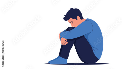 Young man sits alone on the floor and cries while hugging his knees in a moment of deep sadness, loneliness, or depression.