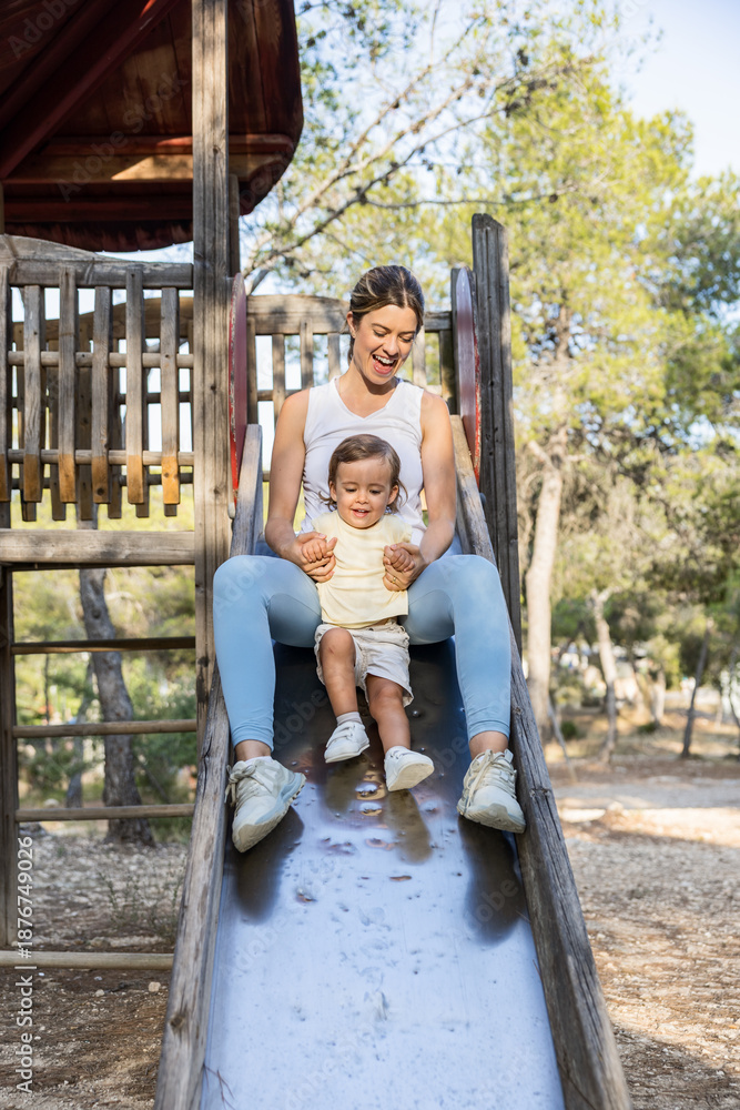 Obraz premium Joyful mother and toddler sliding down a slide at a forest park