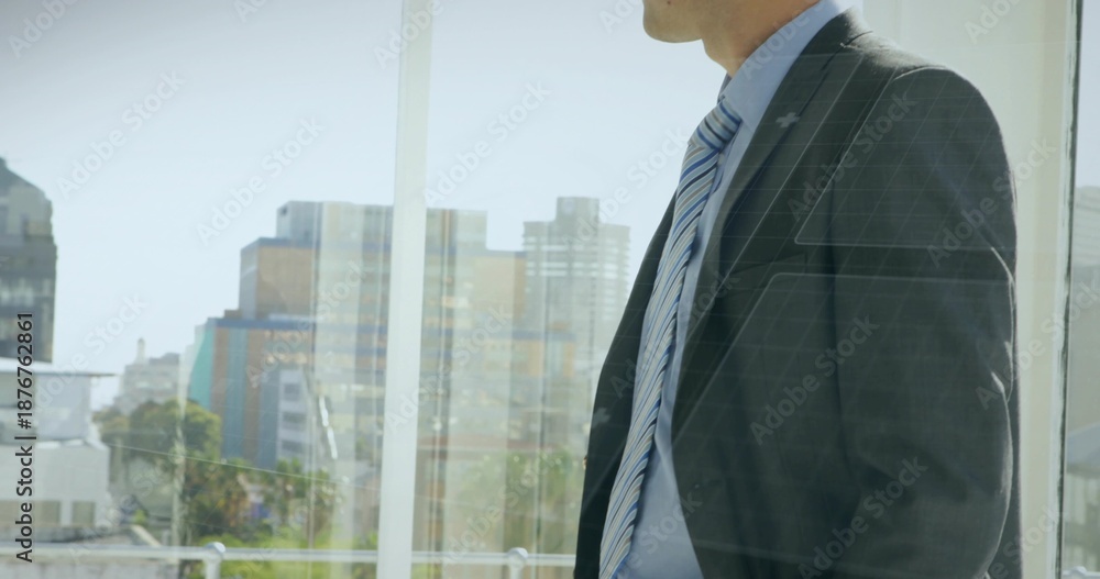Fototapeta premium Standing man in dark suit, striped tie gazing through glass at urban skyline, copy space