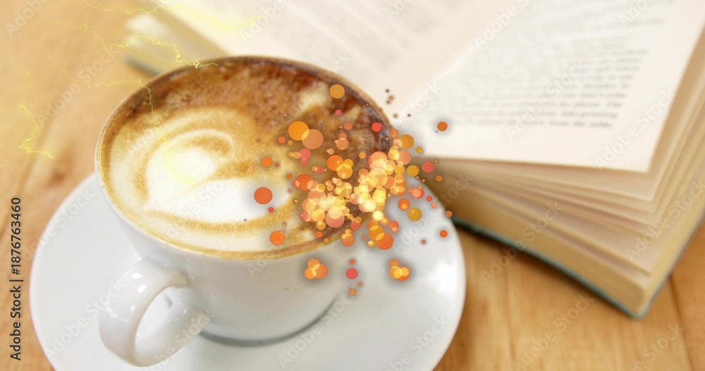 Fototapeta premium Showing white ceramic cup and saucer with latte art on wooden table, paperback, spoon, orange bokeh
