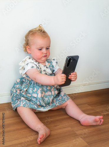A young child is sitting on the floor holding a cell phone
